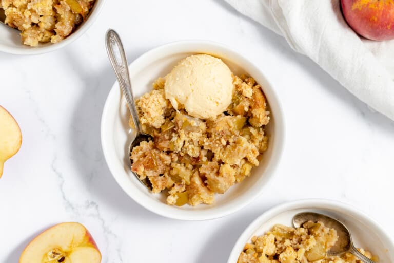 A bowl of peach crisp with ice cream and a scoop of ice cream.