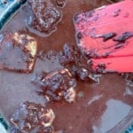 A red spatula is being used to stir chocolate in a pan for chocolate fudge cake.