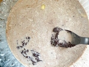 A spoon is being used to stir chocolate fudge into a bowl.