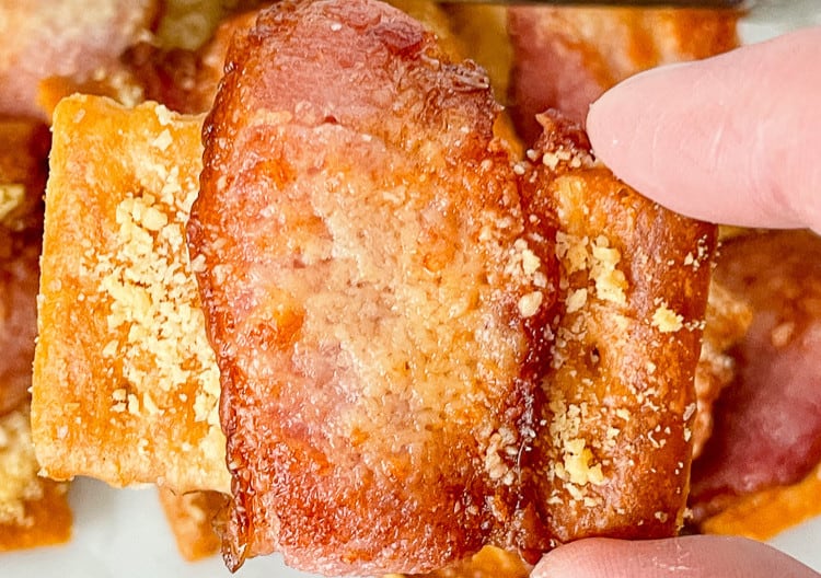 A person holding a piece of bacon on a plate.