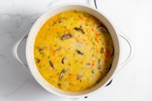 A pot of soup with carrots and mushrooms in it.