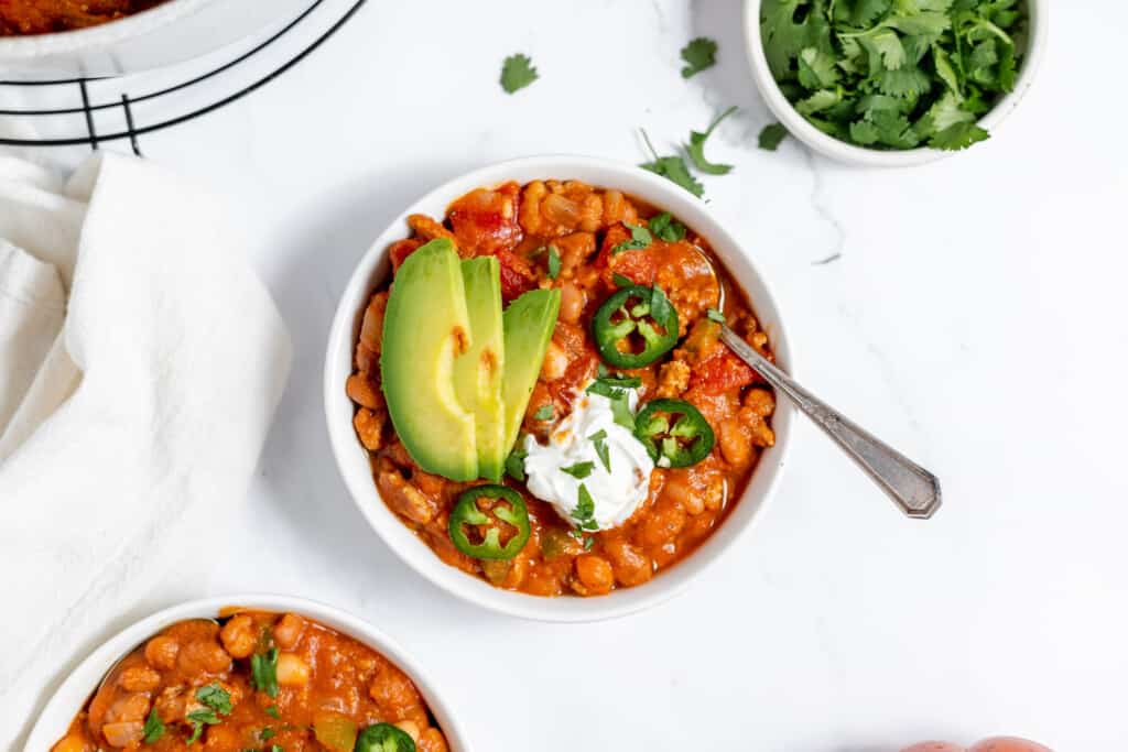 Three bowls of turkey pumpkin chili with avocado and sour cream.