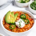 A bowl of turkey pumpkin chili with sour cream and avocado.
