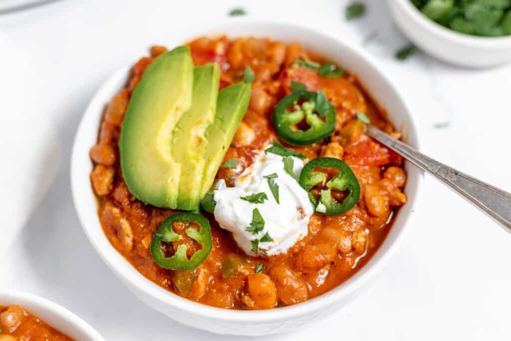 A bowl of turkey pumpkin chili with avocado and sour cream.