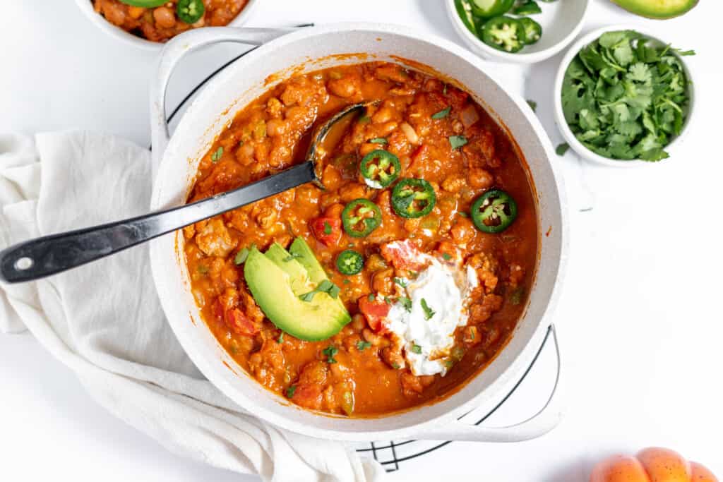 A pot of chili with turkey and pumpkin topped with avocado and sour cream.
