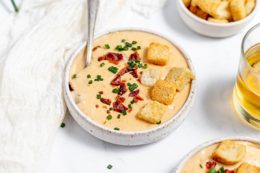 Three bowls of soup with croutons and a glass of beer.