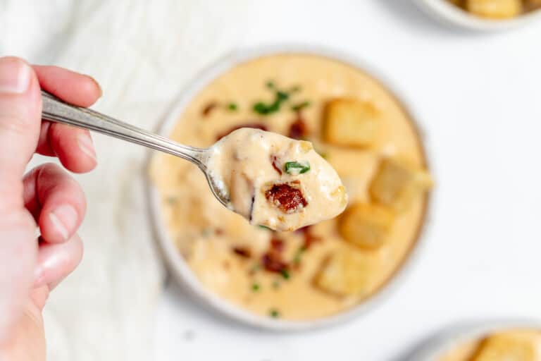 A person holding a spoonful of cheese soup.