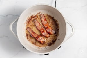 Bacon cooking in a pan on a marble countertop.