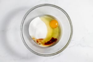 A glass bowl with an egg and sugar in it.
