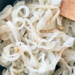 Sliced onions in a pan with a wooden spoon.