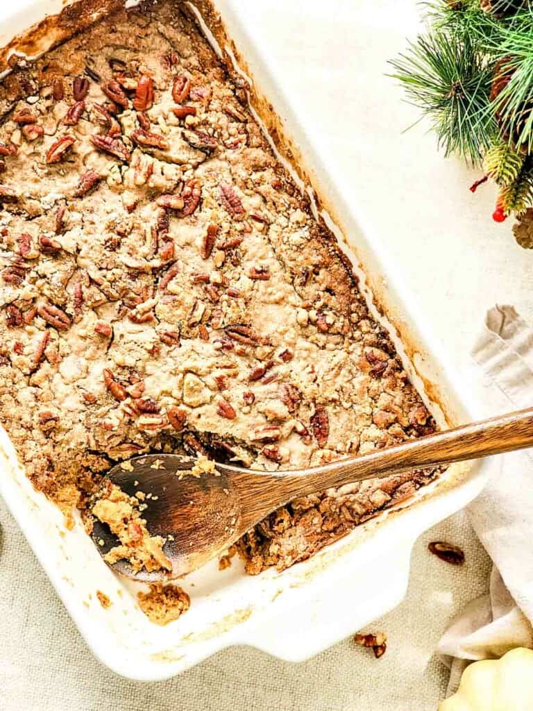 A dish of Sweet Potato Dump Cake with pecans and a wooden spoon.