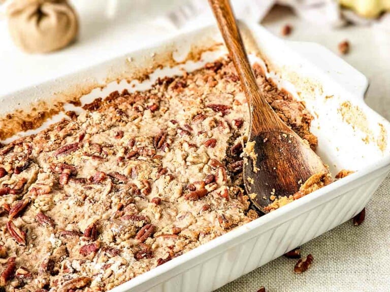 A casserole dish with a wooden spoon sweet potato cake with pecans.