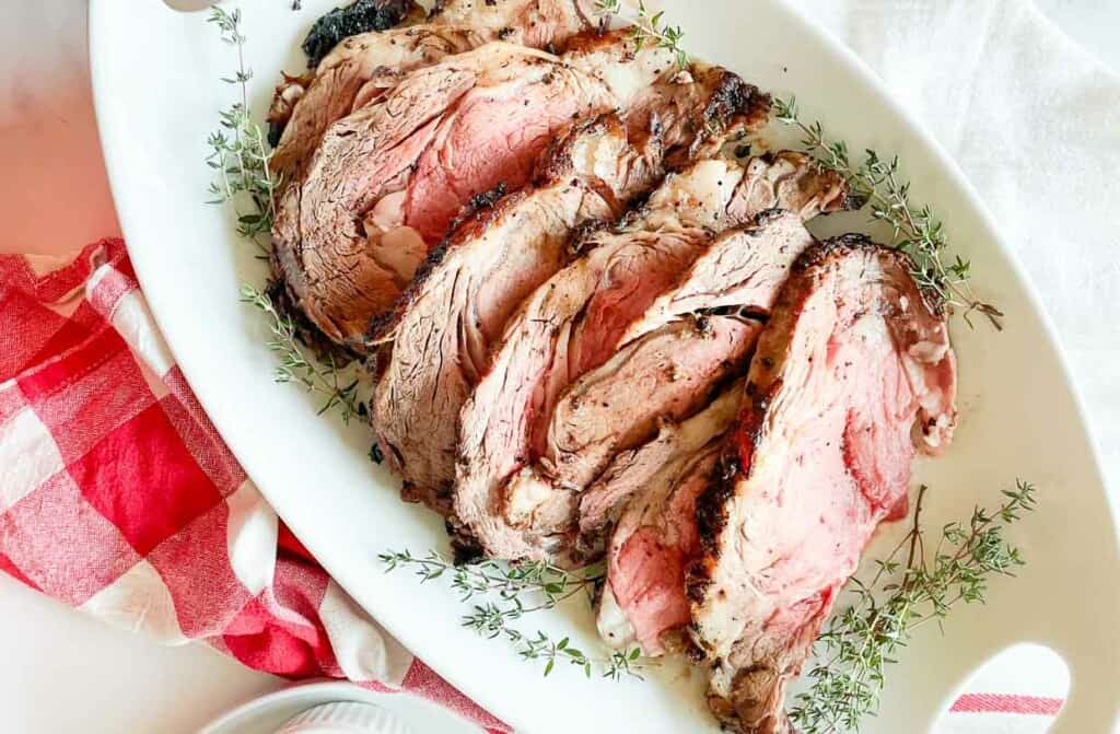 Prime rib roast sliced and arranged on a white plate with sprigs of thyme.