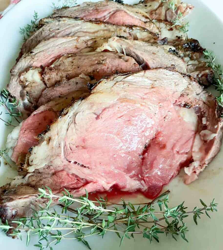 A prime rib roast on a plate with sprigs of thyme.
