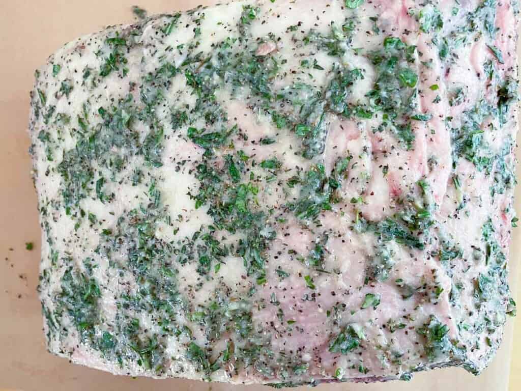 A prime rib roast covered in herbs on a cutting board.