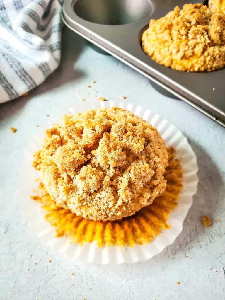 A pumpkin muffin in a muffin tin topped with a delicious crumb topping.