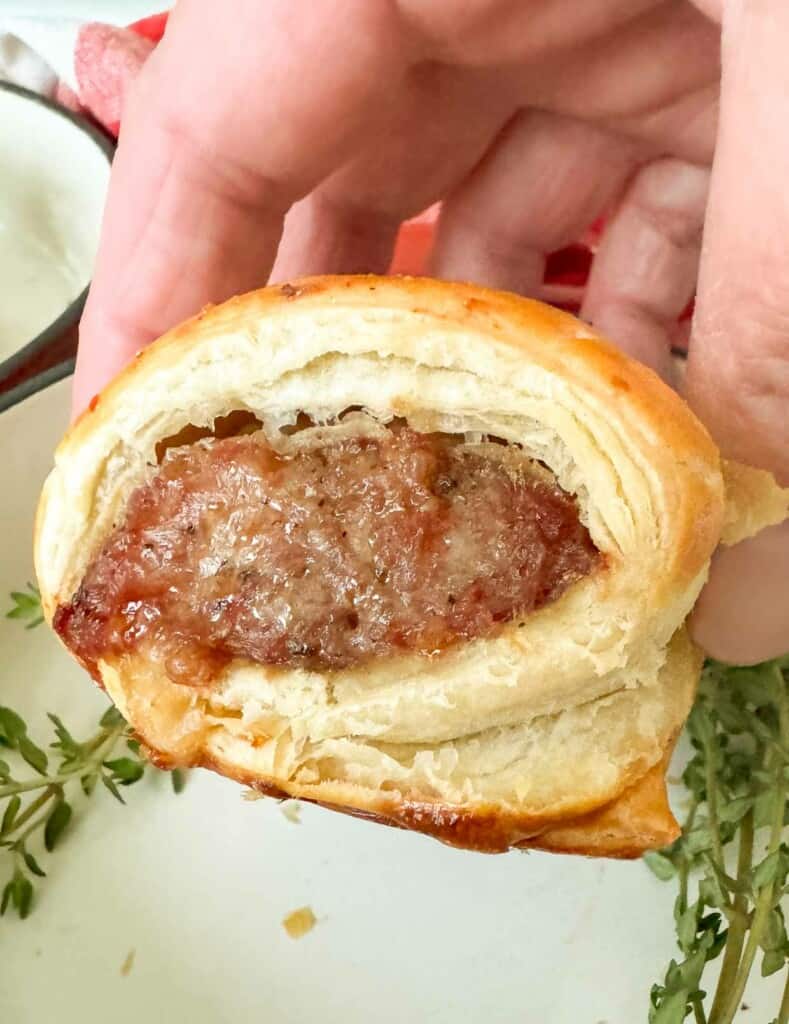 A person holding up a sausage puff pastry.