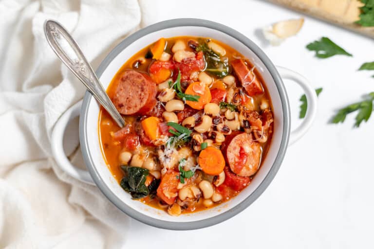 A bowl of white bean and sausage stew with a spoon.