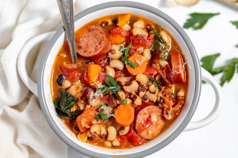 A bowl of soup with sausage, beans and vegetables.