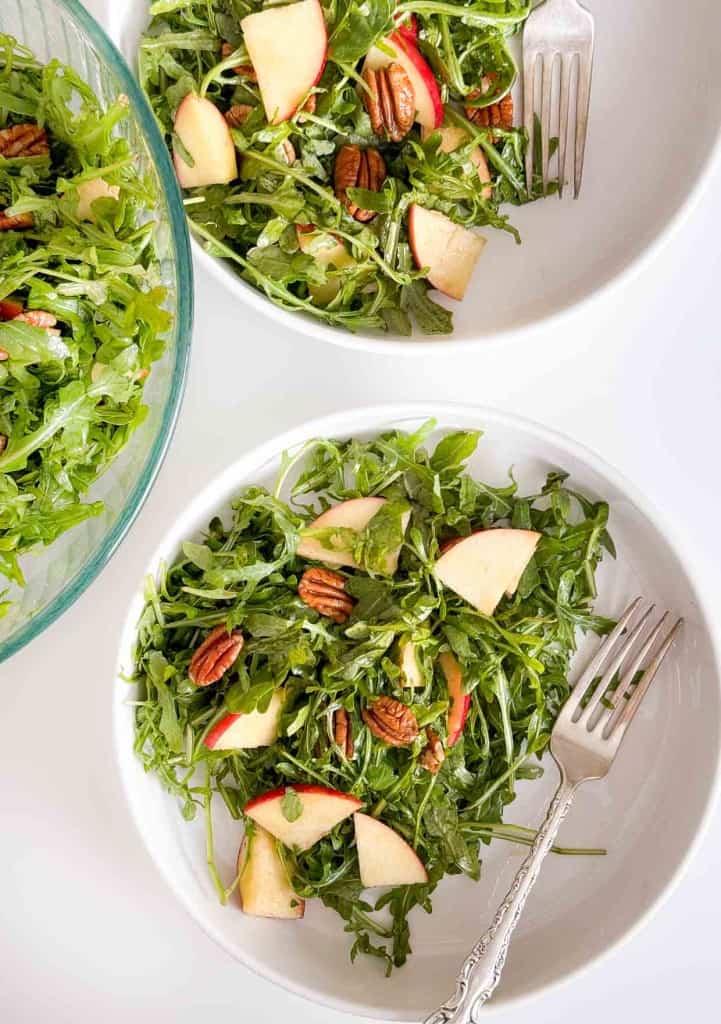 A salad on a plate with apples, pecans, and a fork.