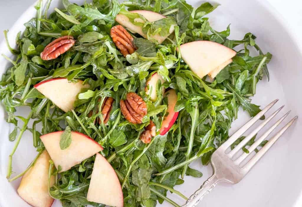 A plate of arugula salad with apples and pecans, perfect for a refreshing and healthy meal.