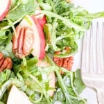 An arugula salad with apples, greens, and pecans on a plate.