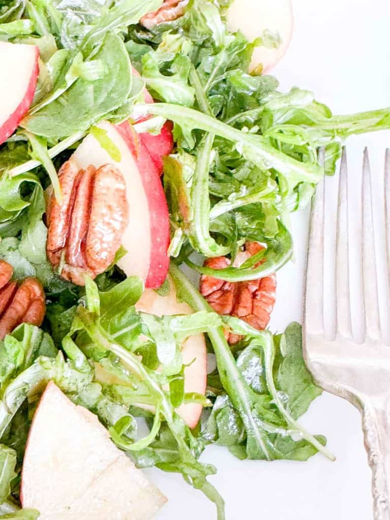 An arugula salad with apples, greens, and pecans on a plate.