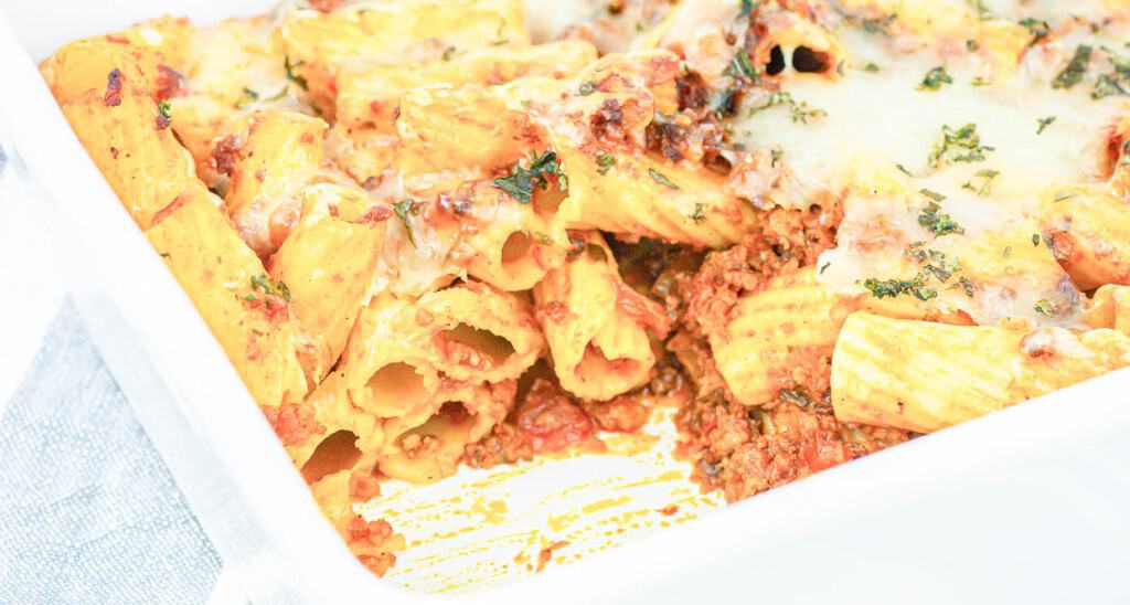 A white dish with pasta and sauce in it.