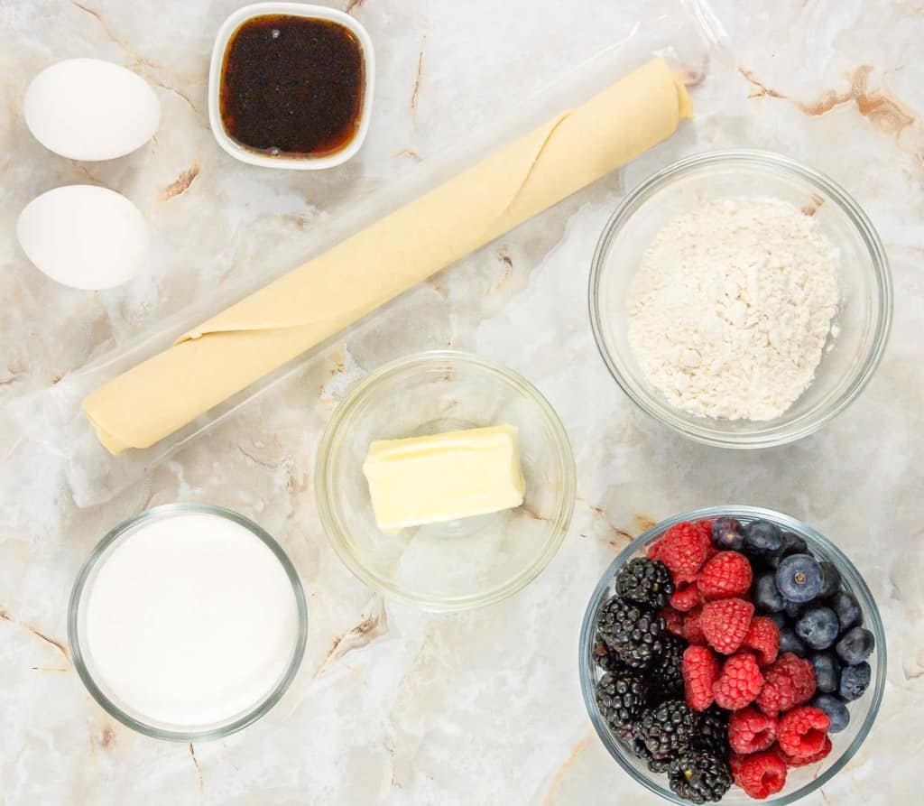 Berries, eggs, butter and flour are laid out on a marble countertop.