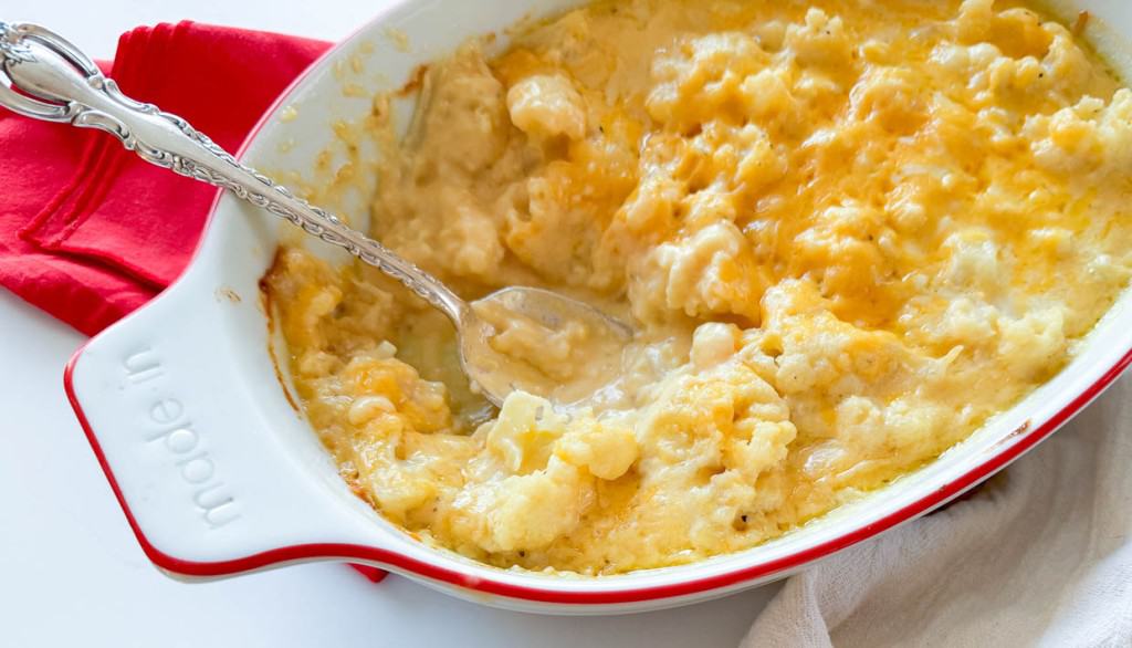 Cheesy cauliflower casserole in a white dish with a spoon.