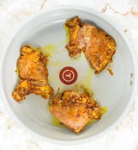 Chicken thighs in a white bowl on a marble countertop.
