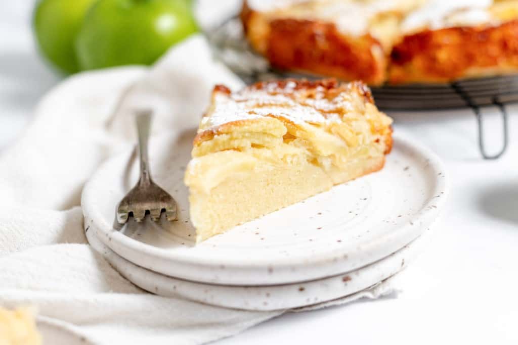 A slice of apple cake on a plate with a fork.