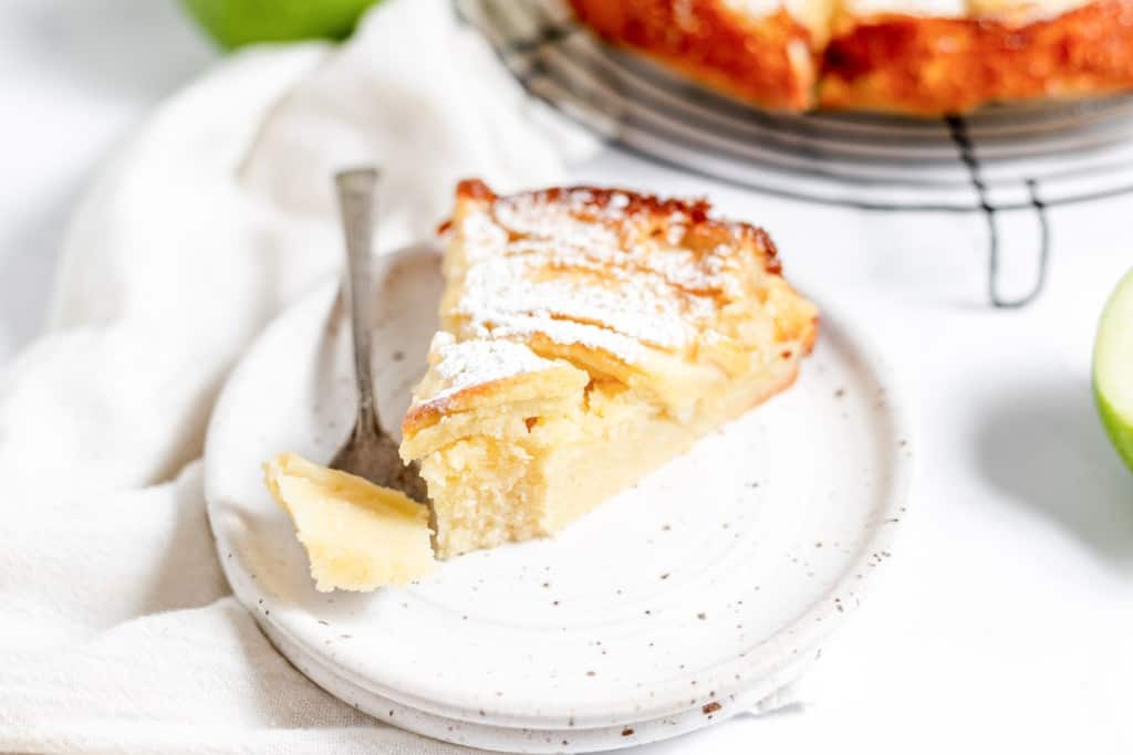 A slice of apple cake with powdered sugar on a plate.
