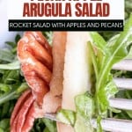 Close-up of a fresh arugula salad, featuring pecan halves and crisp apple slices, with a text overlay that reads "Pecan Apple Arugula Salad.