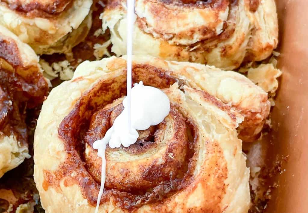 Cinnamon rolls are being dipped in icing.