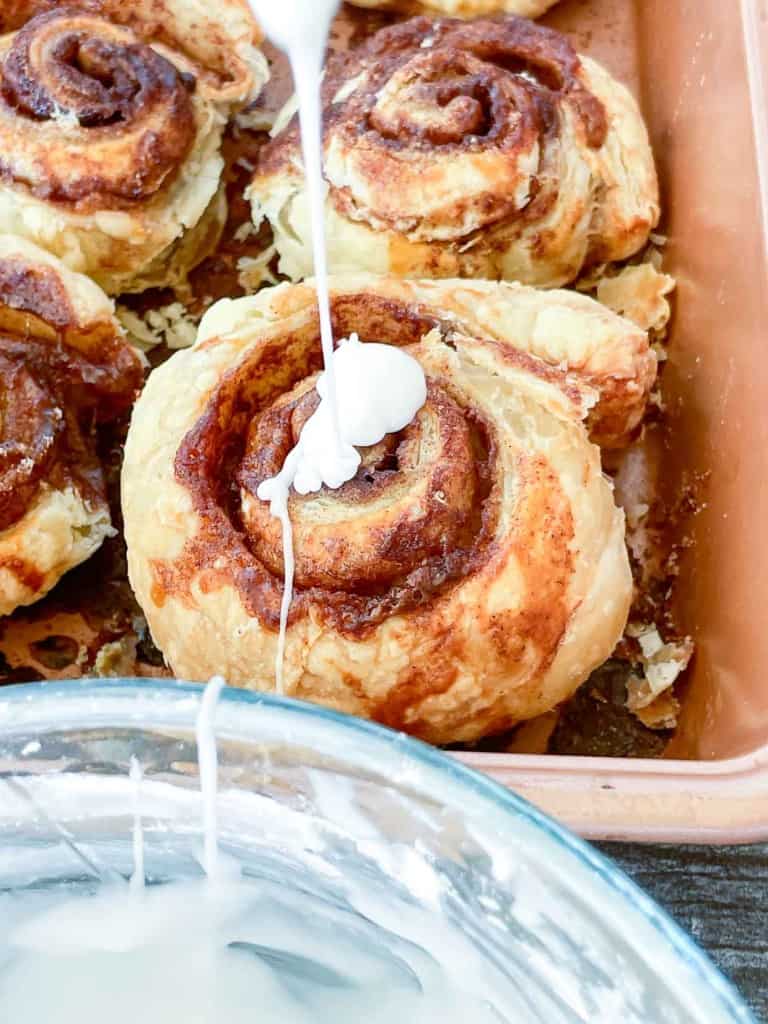 Cinnamon rolls being dipped in icing.