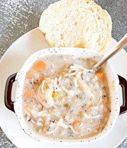 A bowl of chicken soup on a plate with bread.