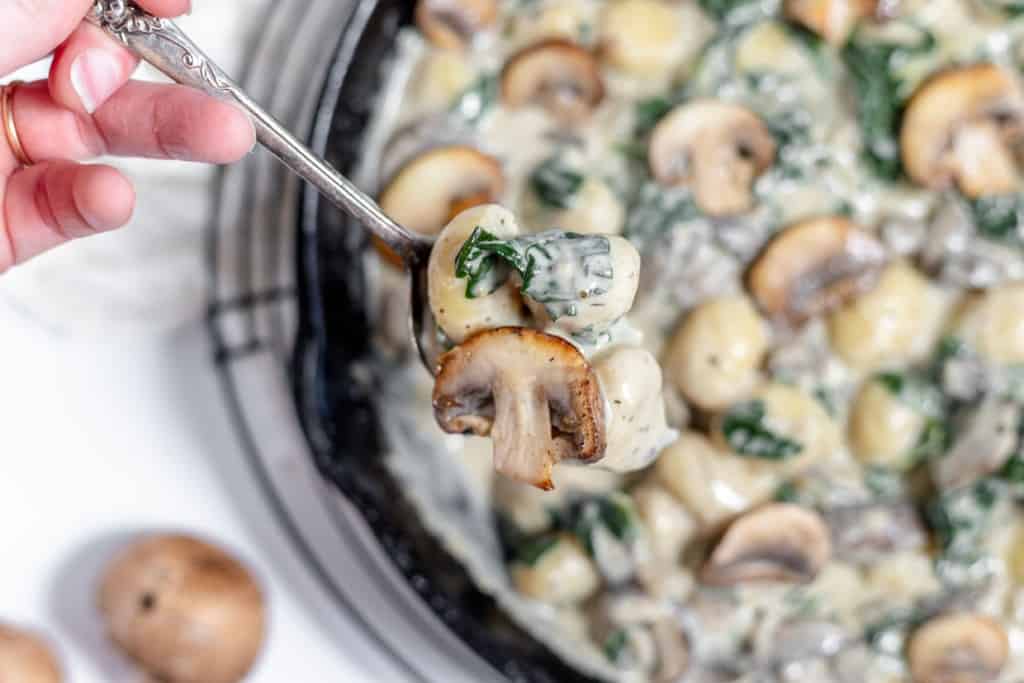 A person holding a fork over a skillet full of spinach and mushrooms.