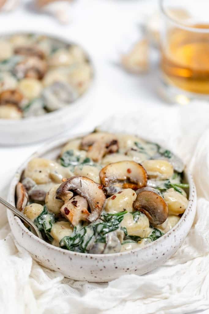 Mushroom and spinach gnocchi in a white bowl with a spoon.