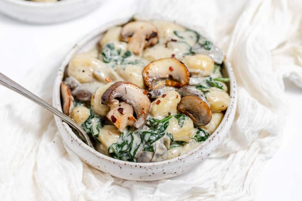 A bowl of pasta with spinach and mushrooms.
