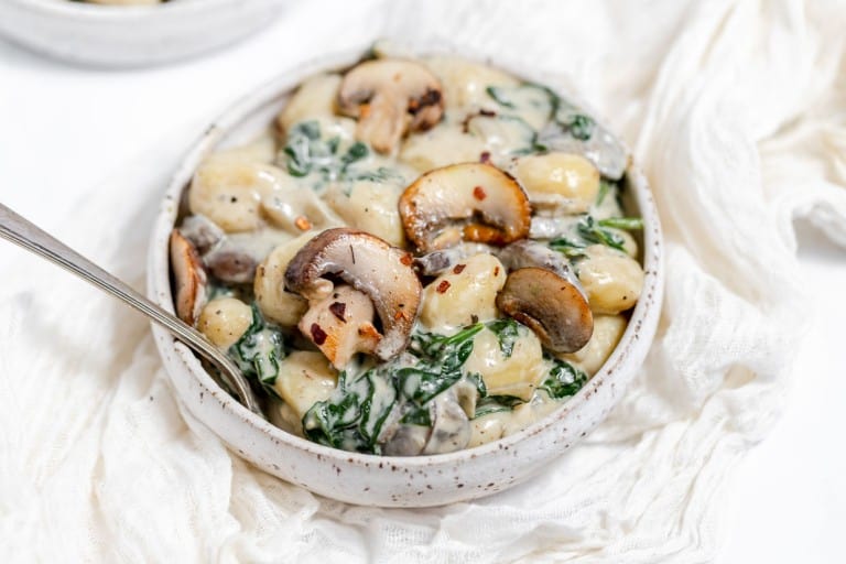 A bowl of pasta with spinach and mushrooms.