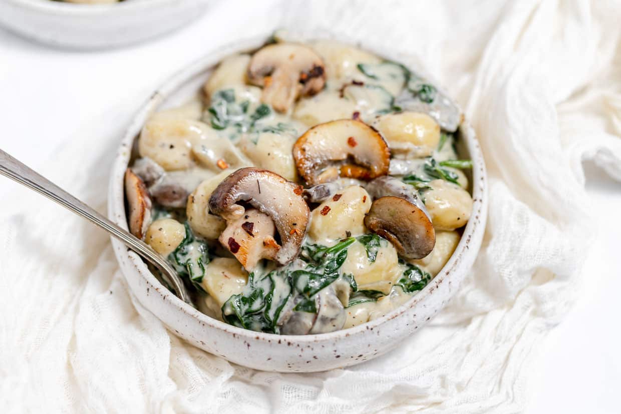 A bowl of pasta with spinach and mushrooms.