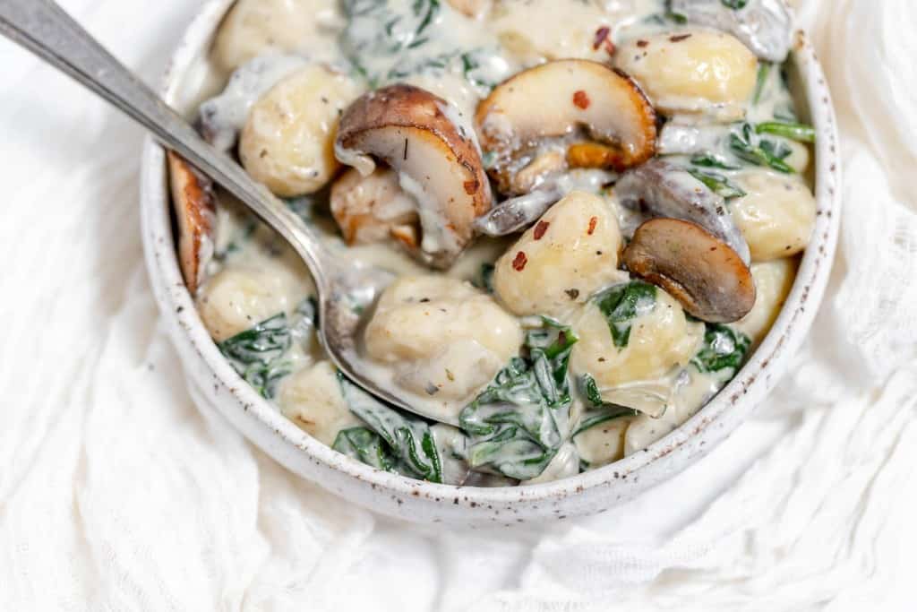 A bowl of spinach and mushroom dumplings with a spoon.