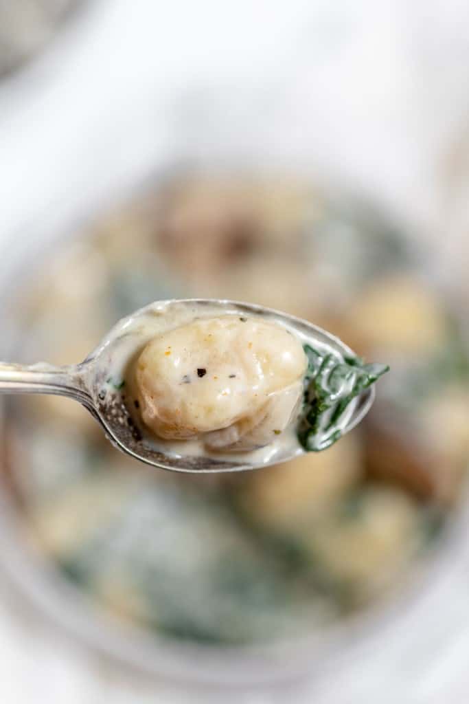 A spoon full of soup with spinach and dumplings.