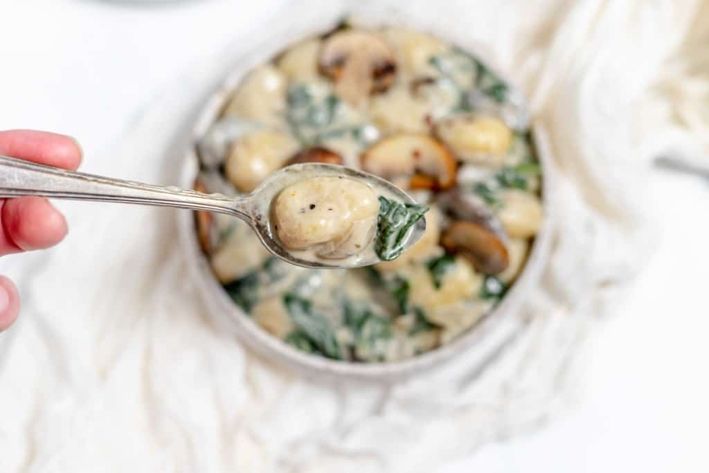 A person is holding a spoon full of spinach and mushrooms.