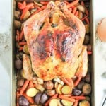 A roasted chicken with carrots and potatoes in a baking pan.