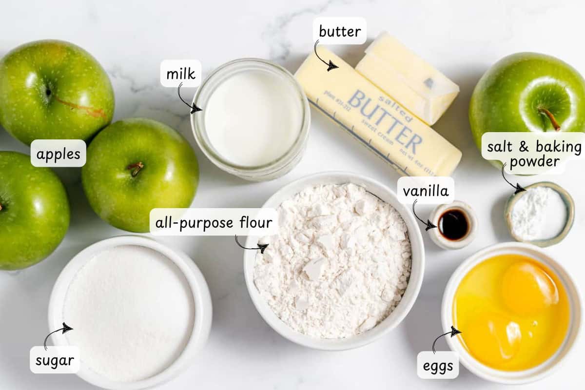 Ingredients for baking a French apple cake include apples, sugar, milk, all-purpose flour, butter, eggs, vanilla, and a bowl labeled salt and baking powder, all neatly arranged on a white surface.