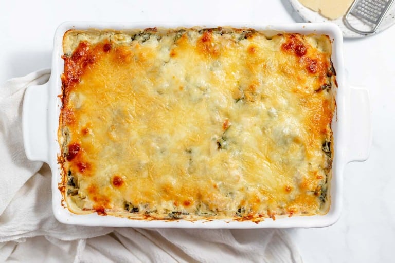 Cheesy spinach lasagna in a white dish.