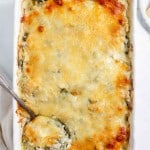 Spinach and cheese casserole in a white dish with a spoon.