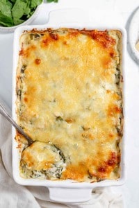 Spinach and cheese casserole in a white dish with a spoon.